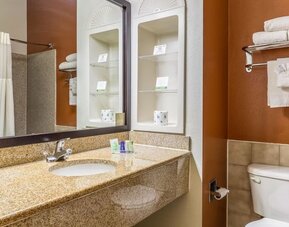 Bathroom with a granite vanity, white sink, large mirror, toiletries, towel rack with folded towels, and toilet at Sleep Inn & Suites Stafford - Sugar Land.