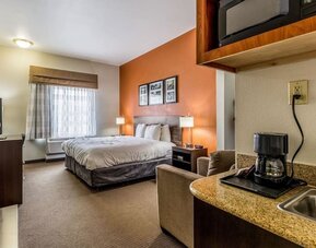 King guest room with a large bed, orange accent wall, framed artwork, bedside lamps, television, armchair, kitchenette counter, and coffee maker at Sleep Inn & Suites Stafford - Sugar Land.