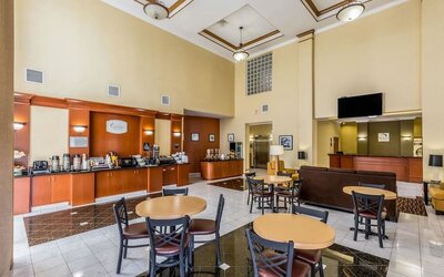 Hotel breakfast and lobby area with a coffee station, dining tables and chairs, reception desk, seating area, and polished tile floor at Sleep Inn & Suites Stafford - Sugar Land.