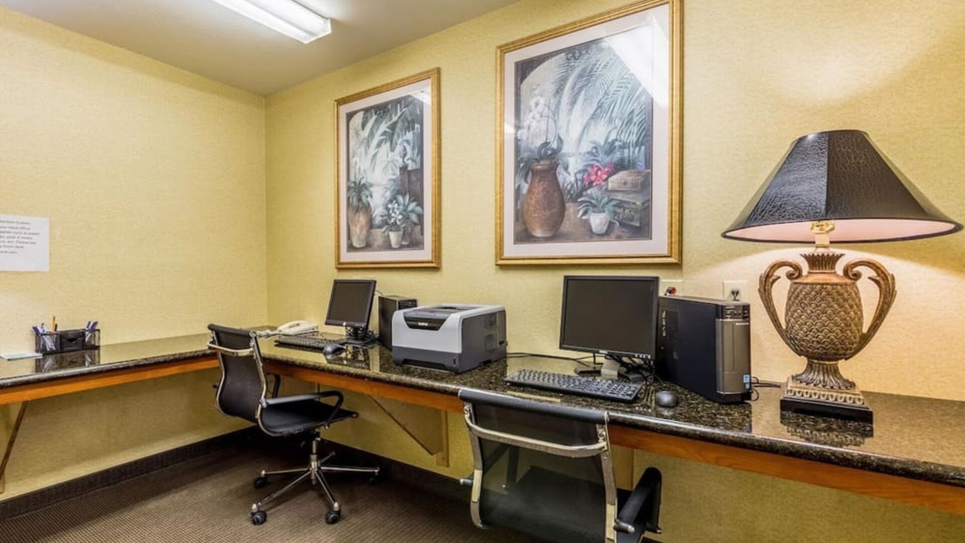 Business center with two computer workstations, monitors, keyboards, office chairs, printer, and decorative artwork at Sleep Inn & Suites Stafford - Sugar Land.