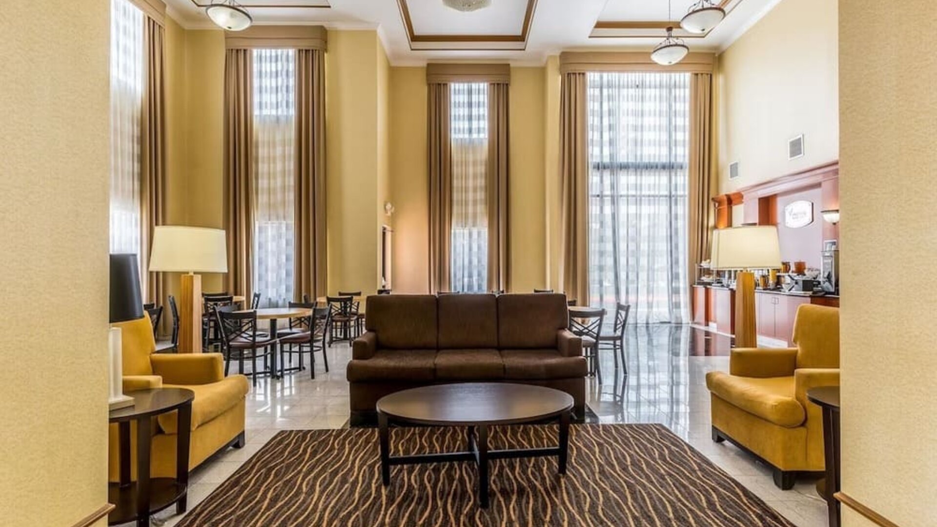 Hotel lobby with a breakfast and coffee station, round dining tables, chairs, sofas, reception area, and high ceilings at Sleep Inn & Suites Stafford - Sugar Land.