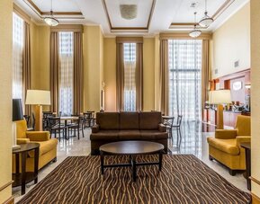 Hotel lobby with a breakfast and coffee station, round dining tables, chairs, sofas, reception area, and high ceilings at Sleep Inn & Suites Stafford - Sugar Land.