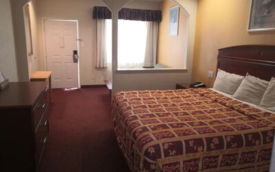 King guest room with a large patterned bed, dark wooden headboard, dresser, television, desk, mirror, and arched wall openings leading to the sitting area at Scottish Inn & Suites.
