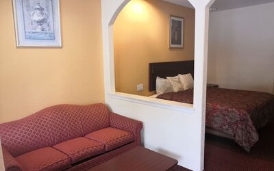 Guest room with a red patterned sofa and coffee table in the sitting area, with a king bed visible through two arched openings at Scottish Inn & Suites.