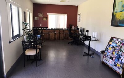 Hotel common area with tables and chairs, a long wooden counter, work desk with computer, beverage station, windows, and a brochure rack at Scottish Inn & Suites.
