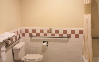 Accessible bathroom with a toilet, bathtub and shower, grab bars, towel racks, and tiled walls at Scottish Inn & Suites.