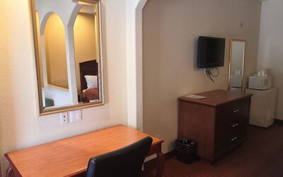 Guest room workspace with a wooden desk and chair, wall mirror, television, dresser, microwave, and mini refrigerator at Scottish Inn & Suites.