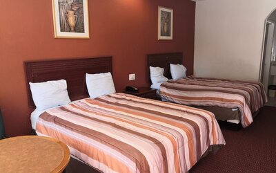Guest room with two beds featuring striped orange, brown, and cream bedspreads, dark wooden headboards, bedside telephone, round table, and framed artwork at Scottish Inn & Suites.