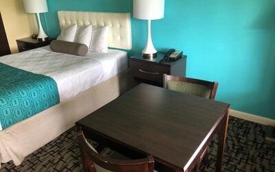 King guest room with a white tufted headboard, white bedding, turquoise patterned bed runner, dark bedside tables with lamps and telephone, and a dining table with chairs at Howard Johnson Express Inn - Rocky Hill.