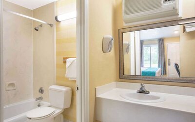 Bathroom with a bathtub and shower, toilet, white vanity with sink, large rectangular mirror, wall-mounted air-conditioning unit, and towel rack at Howard Johnson Express Inn - Rocky Hill.