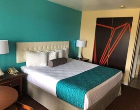 King guest room with white bedding, a tufted headboard, turquoise patterned bed runner, bedside tables with lamps and telephone, and large black and orange geometric wall artwork at Howard Johnson Express Inn - Rocky Hill.
