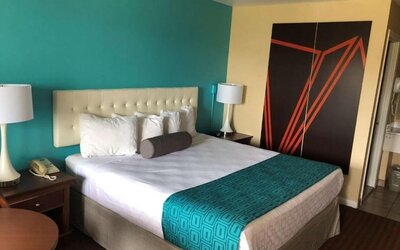King guest room with white bedding, a tufted headboard, turquoise patterned bed runner, bedside tables with lamps and telephone, and large black and orange geometric wall artwork at Howard Johnson Express Inn - Rocky Hill.