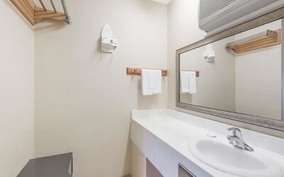 Bathroom vanity with a large rectangular mirror, white countertop and sink, towel rack with folded towels, wall-mounted hairdryer, and air-conditioning unit above the mirror at Howard Johnson Express Inn - Rocky Hill.