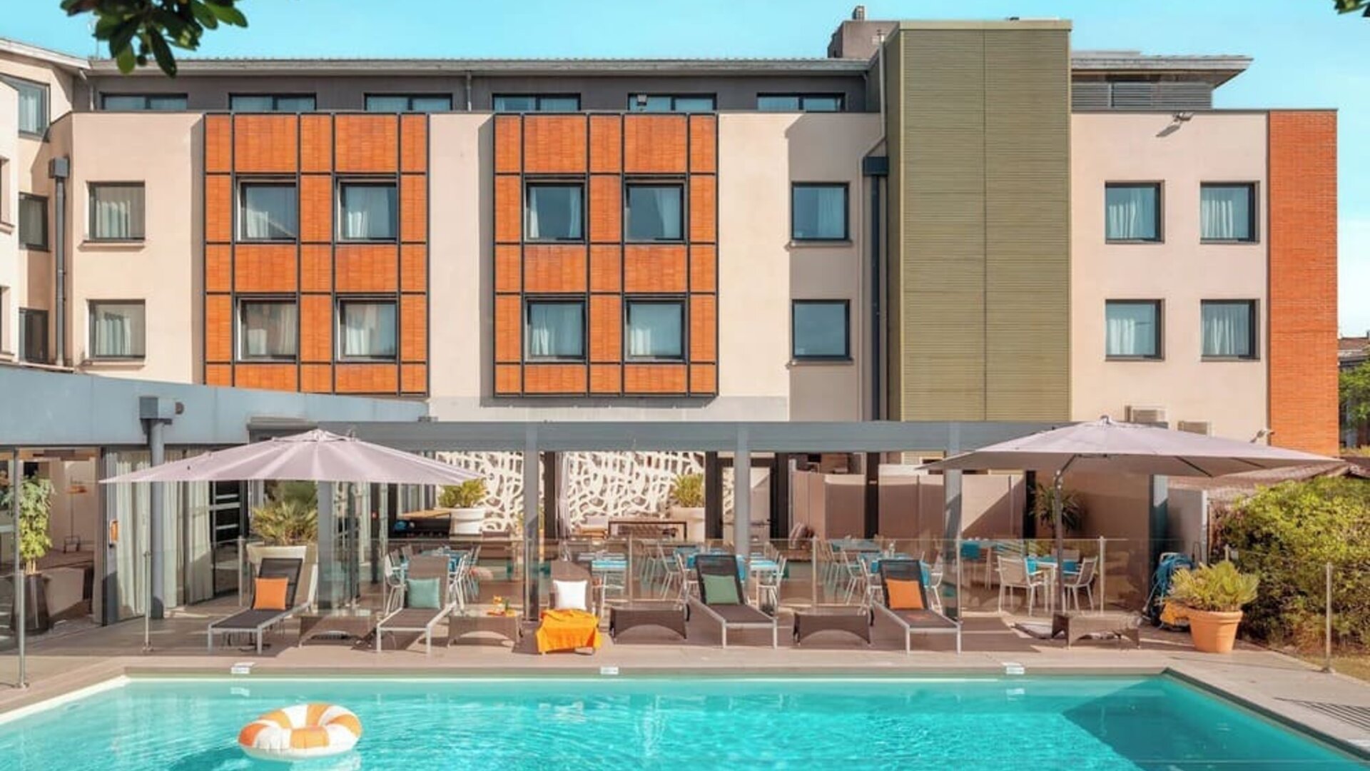 Outdoor swimming pool surrounded by sun loungers, umbrellas, patio seating, and the hotel building at Holiday Inn Toulouse Airport.