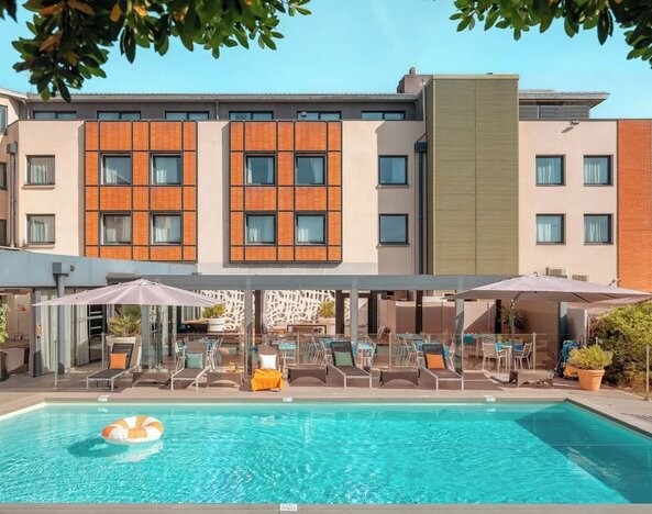 Outdoor swimming pool surrounded by sun loungers, umbrellas, patio seating, and the hotel building at Holiday Inn Toulouse Airport.