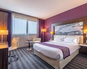 Guest room with a king bed, purple accent wall, airplane artwork, work desk, office chair, and bedside lamps at Holiday Inn Toulouse Airport.