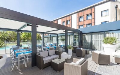 Outdoor terrace with lounge seating, dining tables, glass walls, and views of the hotel pool at Holiday Inn Toulouse Airport.