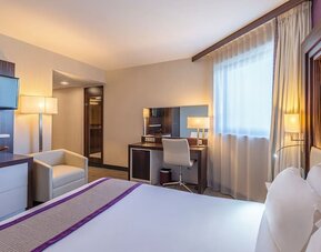 Guest room with a king bed, TV, armchair, work desk, bedside tables, and purple accent wall at Holiday Inn Toulouse Airport.