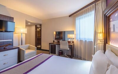 Guest room with a king bed, TV, armchair, work desk, bedside tables, and purple accent wall at Holiday Inn Toulouse Airport.