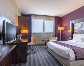 Guest room with a king bed, TV, work desk, armchair, wardrobe, and purple accent wall at Holiday Inn Toulouse Airport.