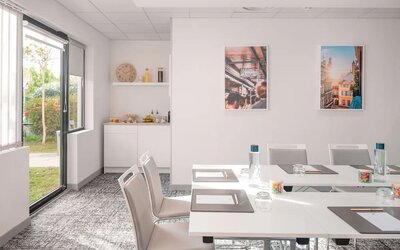 Meeting room with white tables and chairs, large windows, and a refreshment area at Holiday Inn Toulouse Airport.