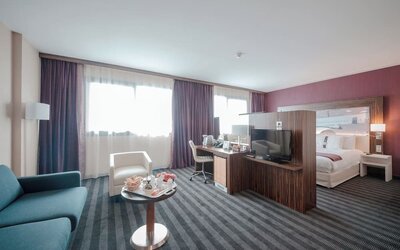 Spacious guest room with a king bed, separate seating area, sofa, coffee table, work desk, and large windows at Holiday Inn Toulouse Airport.