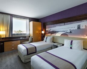 Guest room with two single beds, purple accents, airplane artwork, TV, work desk, and wardrobe at Holiday Inn Toulouse Airport.