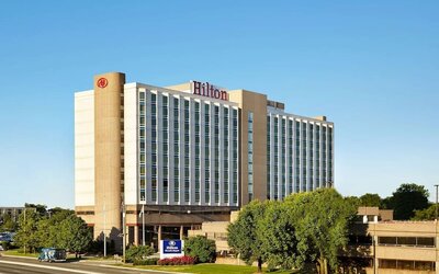 Exterior of Hilton Newark Airport with a multi-story facade, landscaped grounds, entrance driveway, and Hilton signage.
