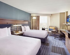 1. Guest room with two double beds, blue accent wall, bedside table, work desk, lounge chair, television, and large windows at Hilton Newark Airport.