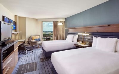Guest room with two double beds, a blue accent wall, work desk, lounge chair, television, and large window at Hilton Newark Airport.
