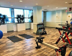 Hotel fitness center with exercise mats, dumbbells, resistance equipment, stationary bikes, rowing machine, and large windows at Hilton Newark Airport.