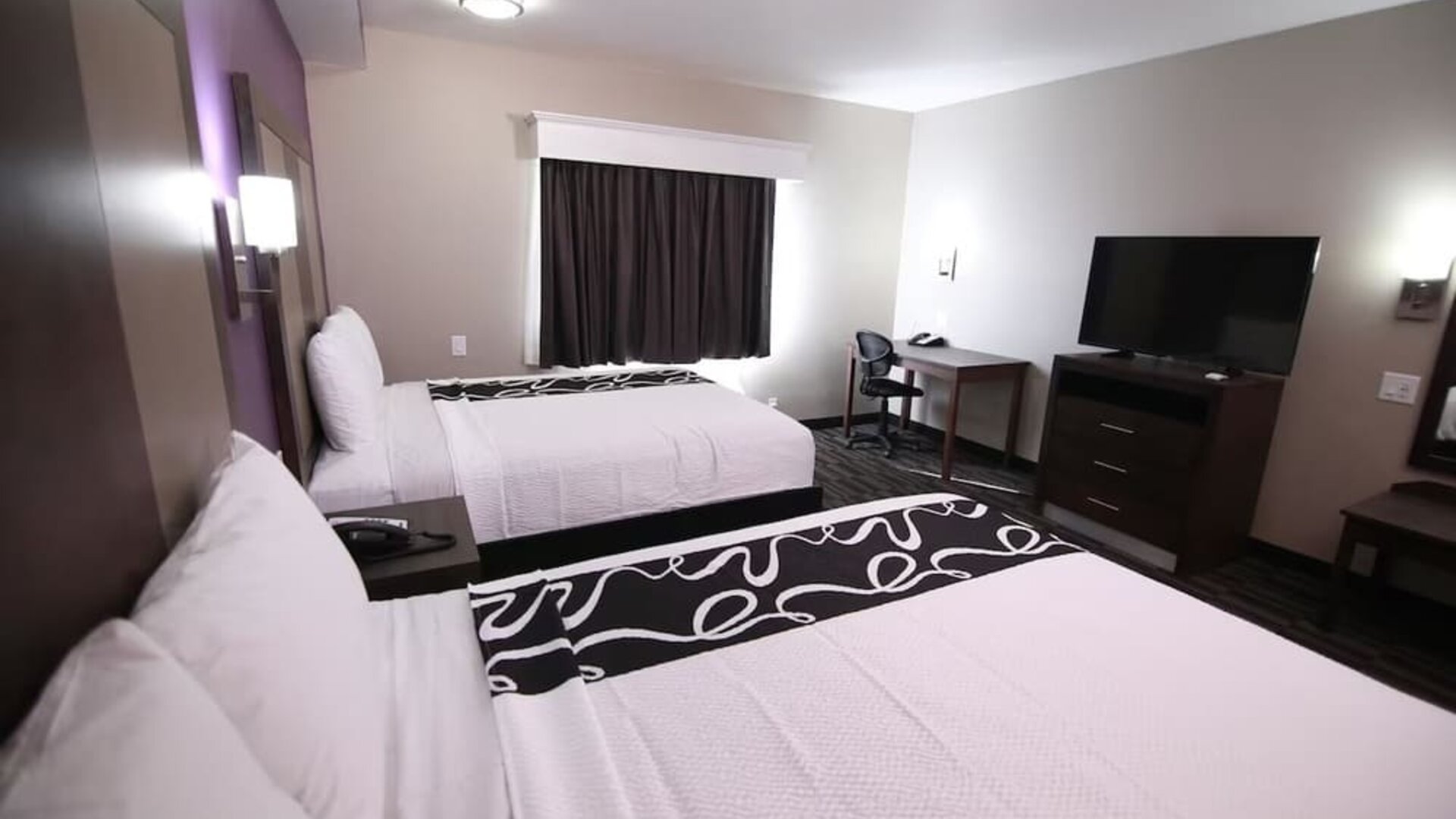 1. Guest room with two beds, white linens, black patterned bed runners, television, desk, dresser, and armchair at At Home Inn & Suites.