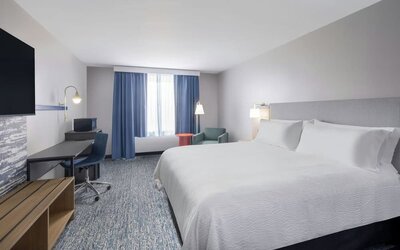1. Spacious guest room with a king bed, white linens, desk and chair, television, seating area, blue curtains, and patterned carpet at Garner by IHG.