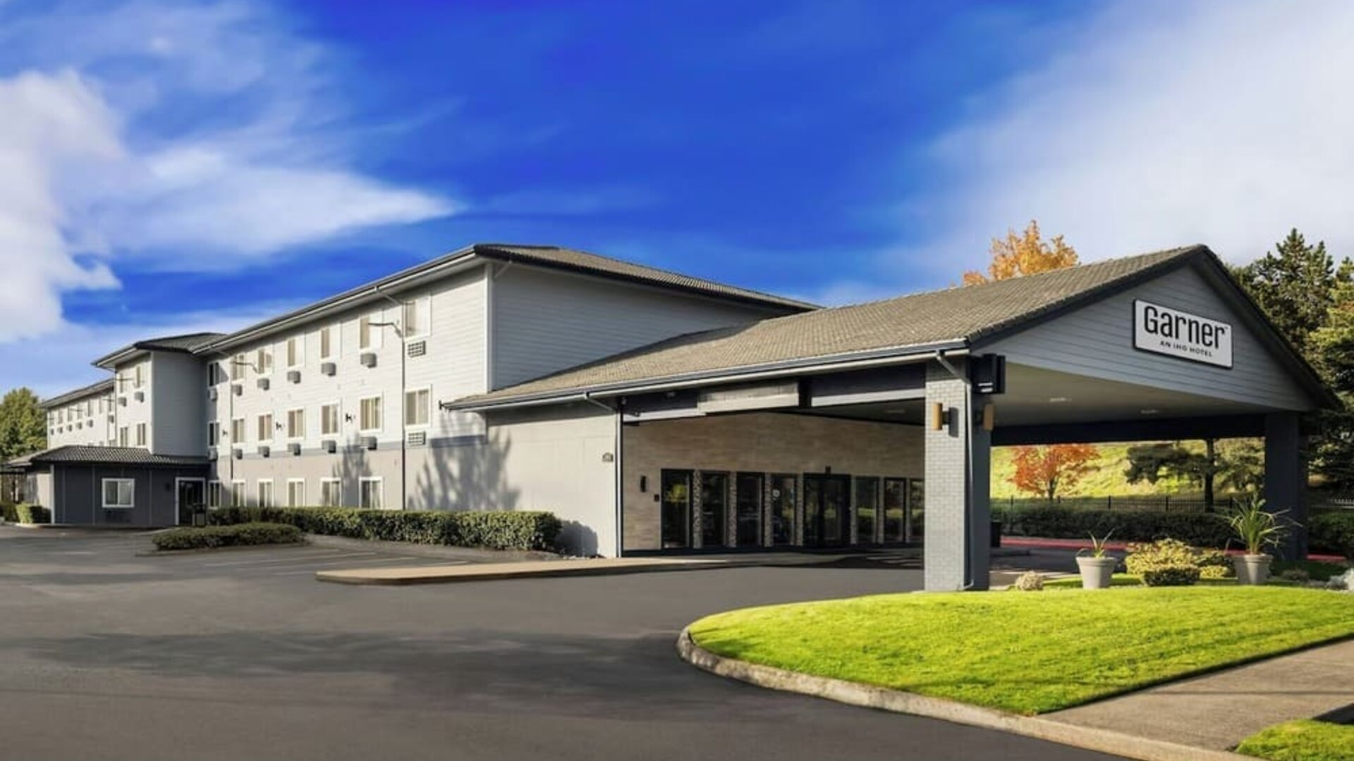 Exterior of Garner by IHG showing the hotel building, covered entrance, landscaped lawn, and parking area.