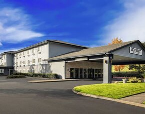 Exterior of Garner by IHG showing the hotel building, covered entrance, landscaped lawn, and parking area.