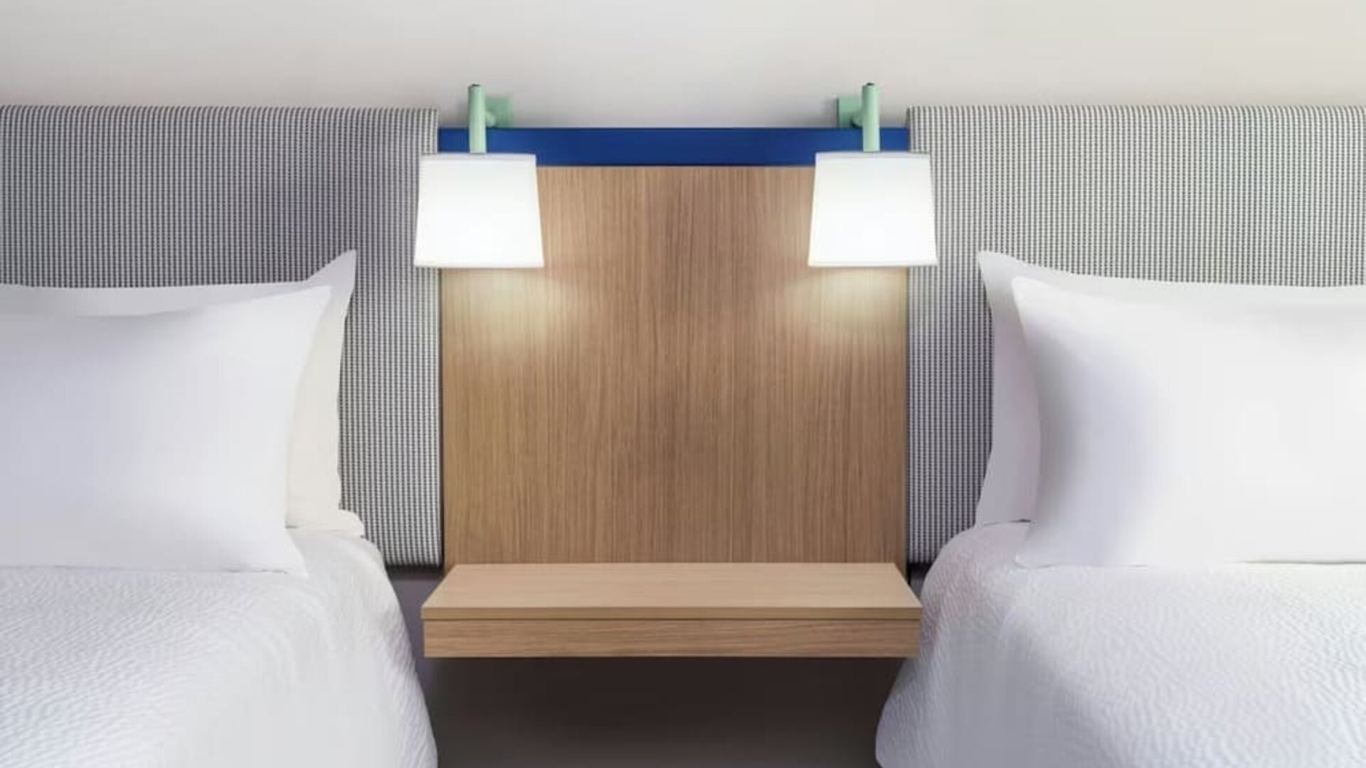 Two hotel beds with white linens, upholstered headboards, wood nightstand, and wall-mounted reading lamps at Garner by IHG.