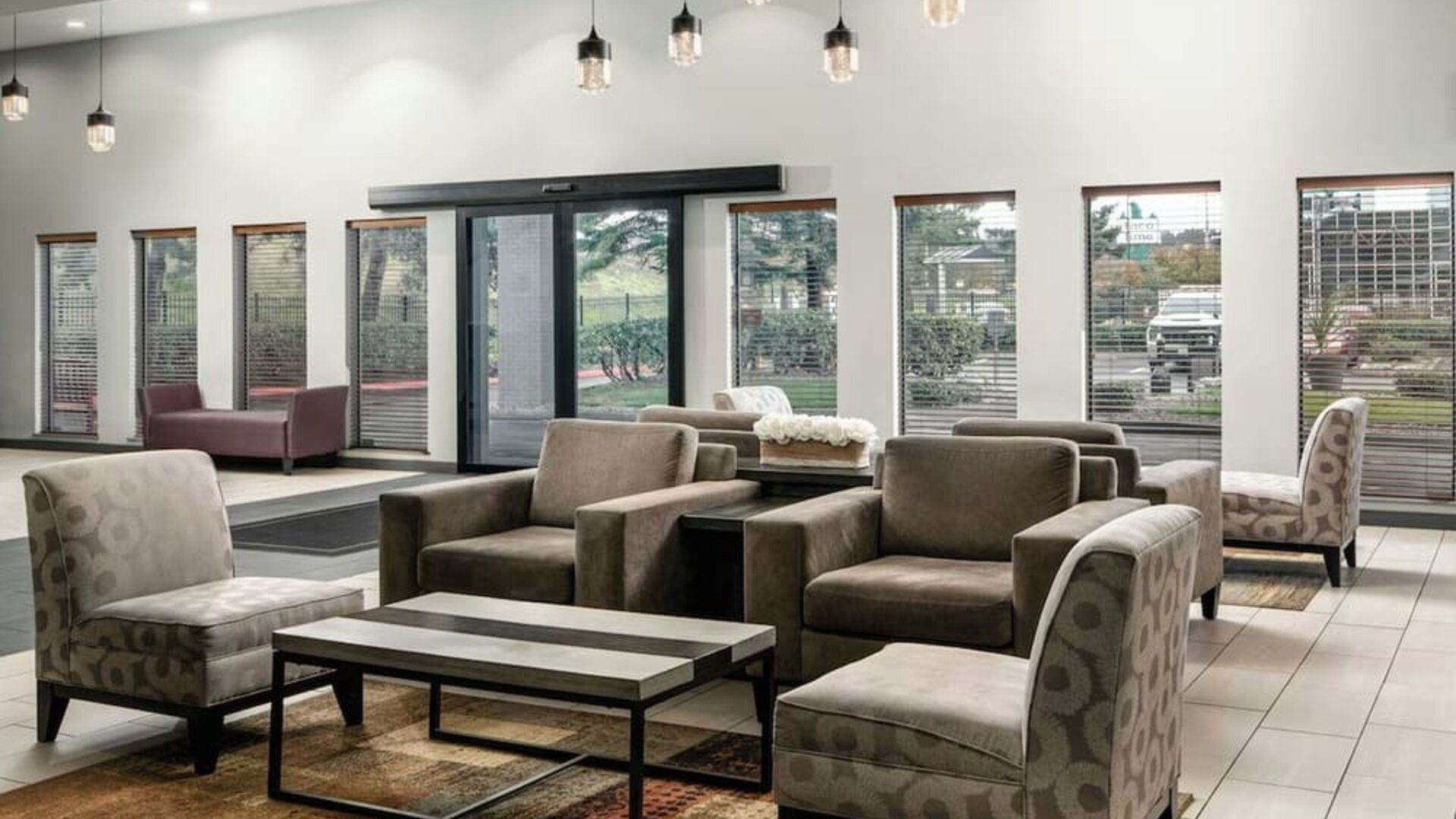 Spacious hotel lobby seating area with upholstered chairs and sofas, large windows, coffee tables, and contemporary decor at Garner by IHG.