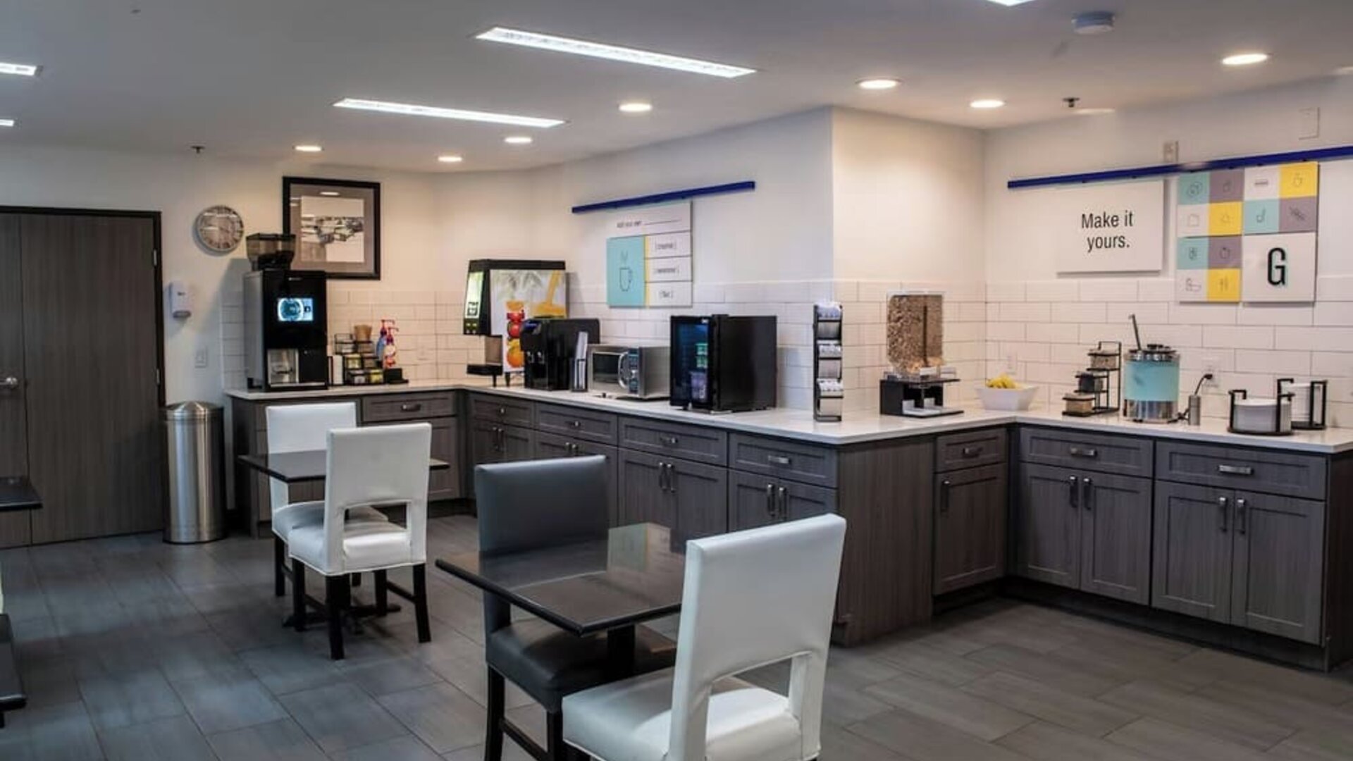Hotel breakfast area with tables and chairs, beverage stations, food counters, and modern cabinetry at Garner by IHG.