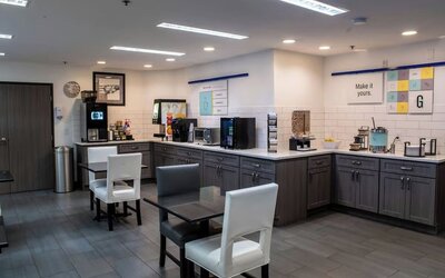 Hotel breakfast area with tables and chairs, beverage stations, food counters, and modern cabinetry at Garner by IHG.