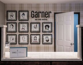 Reception area with a front desk, framed artwork, Garner branding, and IHG One Rewards signage at Garner by IHG.