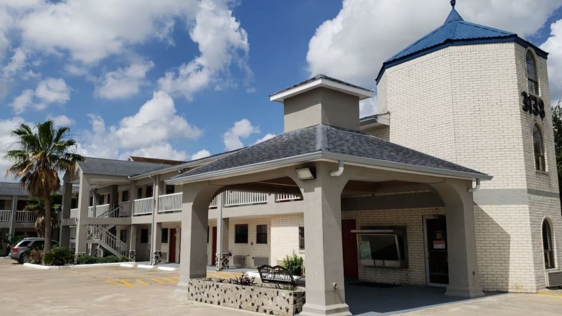Exterior side view of Summit Inn Near Houston Medical Center-NRG Park showing the hotel building, covered walkway, landscaping, and accessible parking.