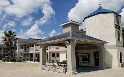 Exterior side view of Summit Inn Near Houston Medical Center-NRG Park showing the hotel building, covered walkway, landscaping, and accessible parking.