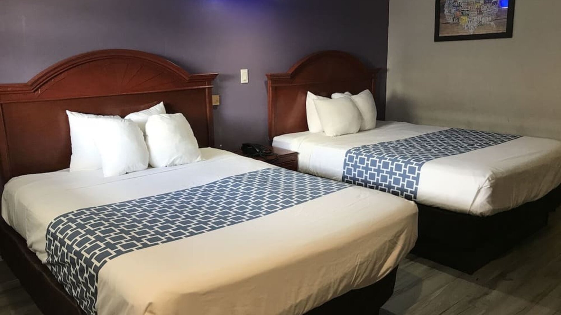 Guest room with two beds featuring white linens, dark wood headboards, patterned blue bed runners, and a purple accent wall at Summit Inn Near Houston Medical Center-NRG Park.