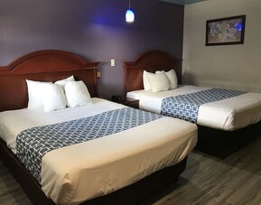 Guest room with two beds featuring white linens, dark wood headboards, patterned blue bed runners, and a purple accent wall at Summit Inn Near Houston Medical Center-NRG Park.