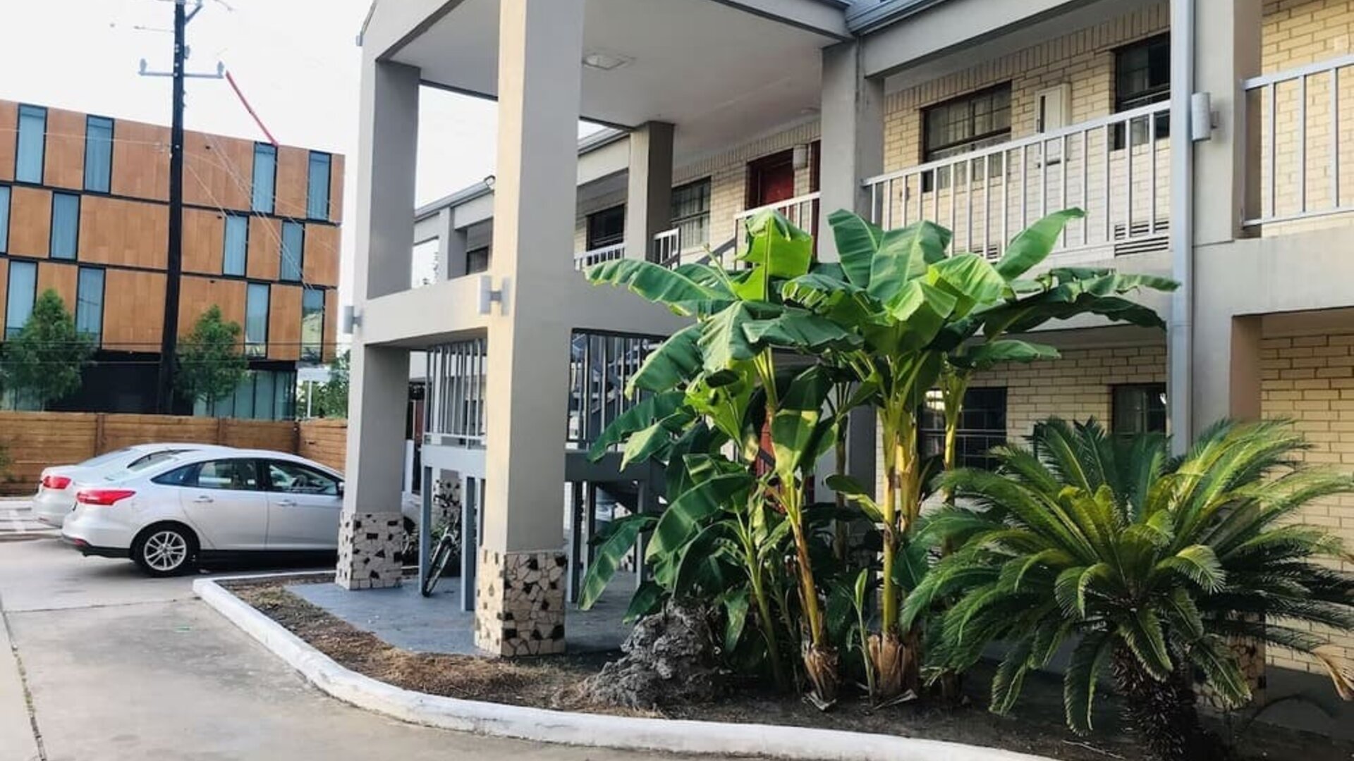 1. Hotel entrance with a covered porte-cochère, white brick exterior, blue roof, arched columns, and parking area at Summit Inn Near Houston Medical Center-NRG Park.