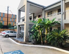 1. Hotel entrance with a covered porte-cochère, white brick exterior, blue roof, arched columns, and parking area at Summit Inn Near Houston Medical Center-NRG Park.