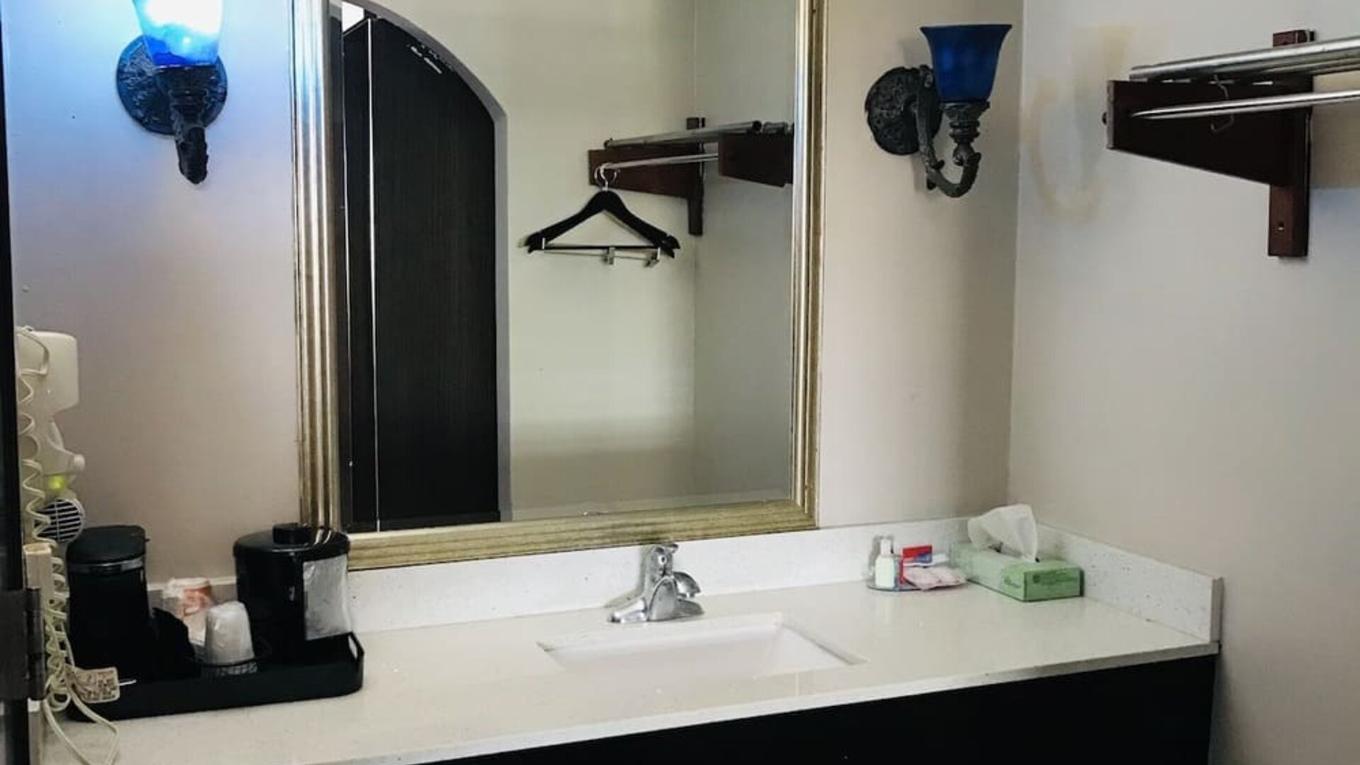 Bathroom vanity with a large framed mirror, white countertop, integrated sink, wall-mounted towel rack, and decorative blue wall sconces at Summit Inn Near Houston Medical Center-NRG Park.