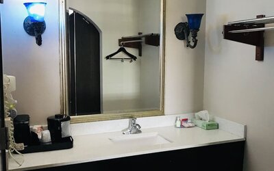Bathroom vanity with a large framed mirror, white countertop, integrated sink, wall-mounted towel rack, and decorative blue wall sconces at Summit Inn Near Houston Medical Center-NRG Park.