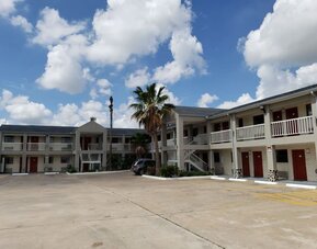 Exterior of Summit Inn Near Houston Medical Center-NRG Park showing the two-story hotel building, exterior corridors, red doors, parking area, and palm trees.