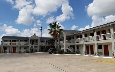 Exterior of Summit Inn Near Houston Medical Center-NRG Park showing the two-story hotel building, exterior corridors, red doors, parking area, and palm trees.